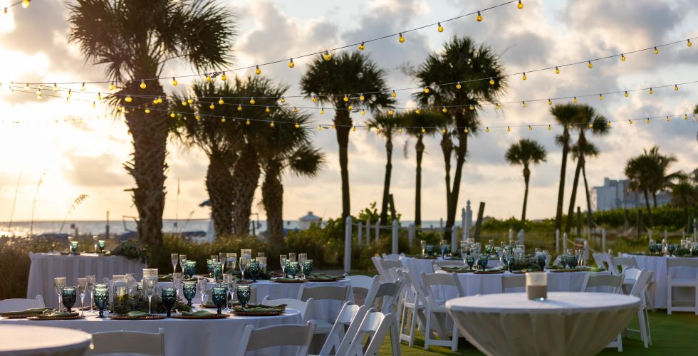A Group Of Tables And Chairs With Palm Trees And A Sunset